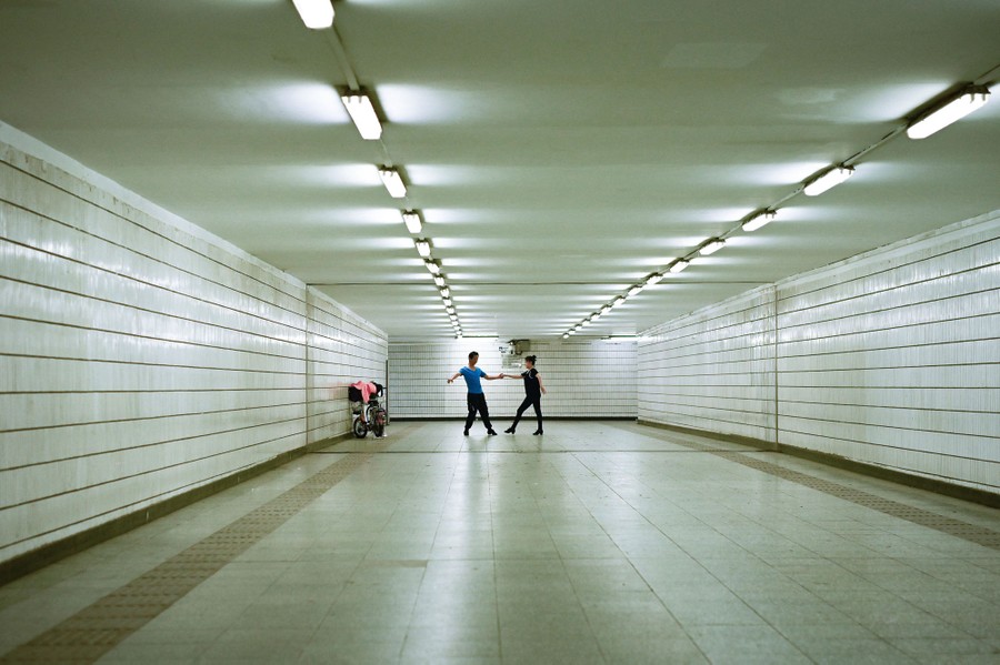 A couple dance in a wide, empty, underground passageway.