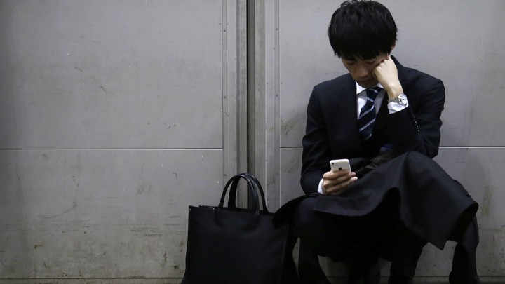 A man leaning against a wall looks down passively at his iPhone