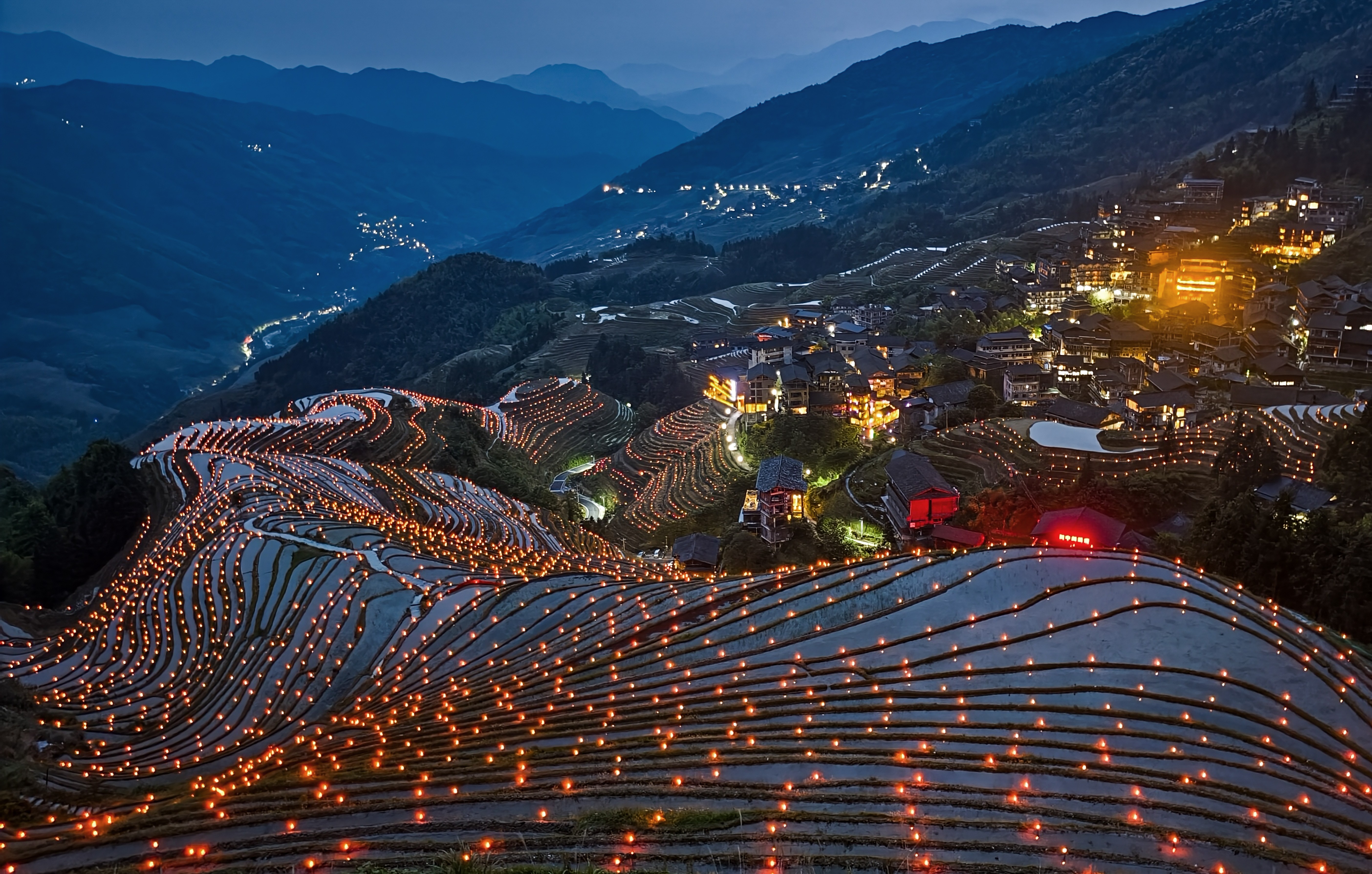 A view, looking down on terraced ricefields with decorative lights set up along the edges.