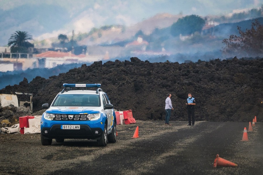 Security officers stand near a lava flow on a road.