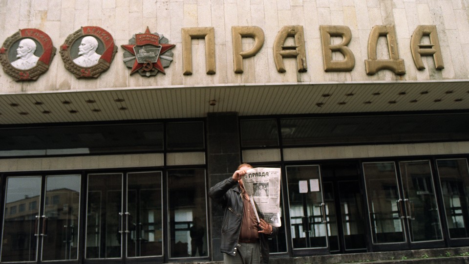 A man shows the headline of the 'Pravda' in front of the entrance of the building of the Soviet newspaper.