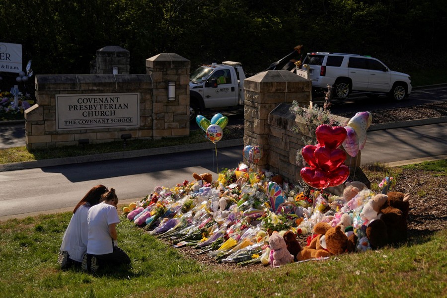 Two people kneel and pray at a makeshift memorial, at the entrance to a school.