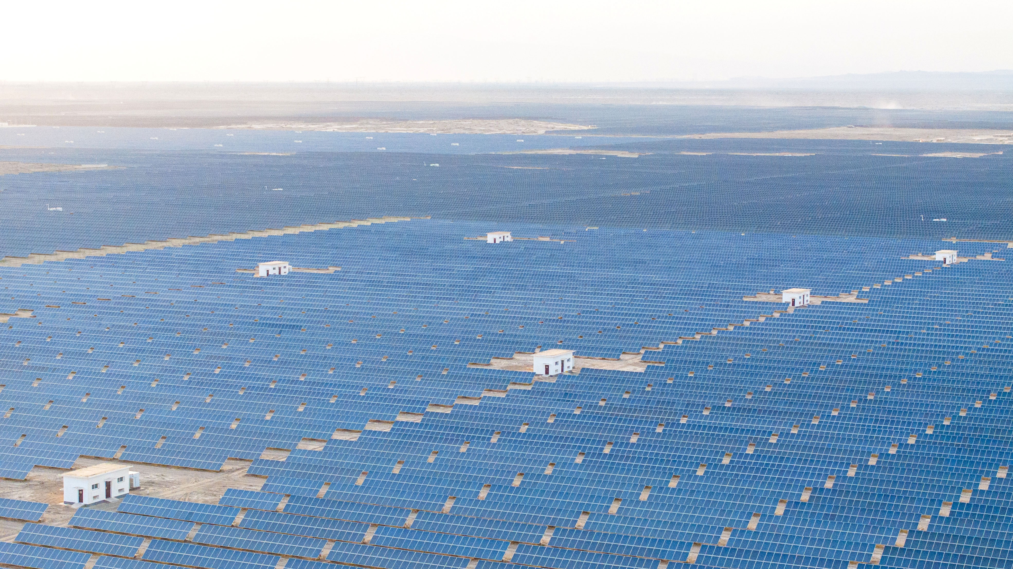 An aerial view—solar panel grids in a desert, stretching to the horizon