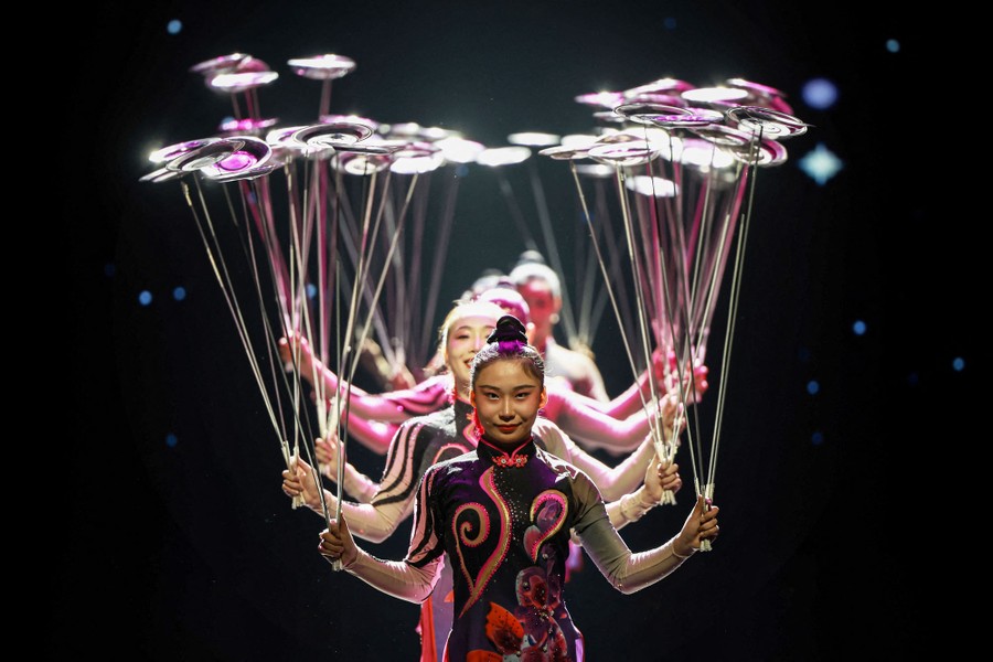 A line of acrobats spin plates atop long sticks.