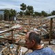 A man in the foreground looks at splinters of structures strewn on the ground amid palm trees after Hurricane Helene struck the Gulf Coast.