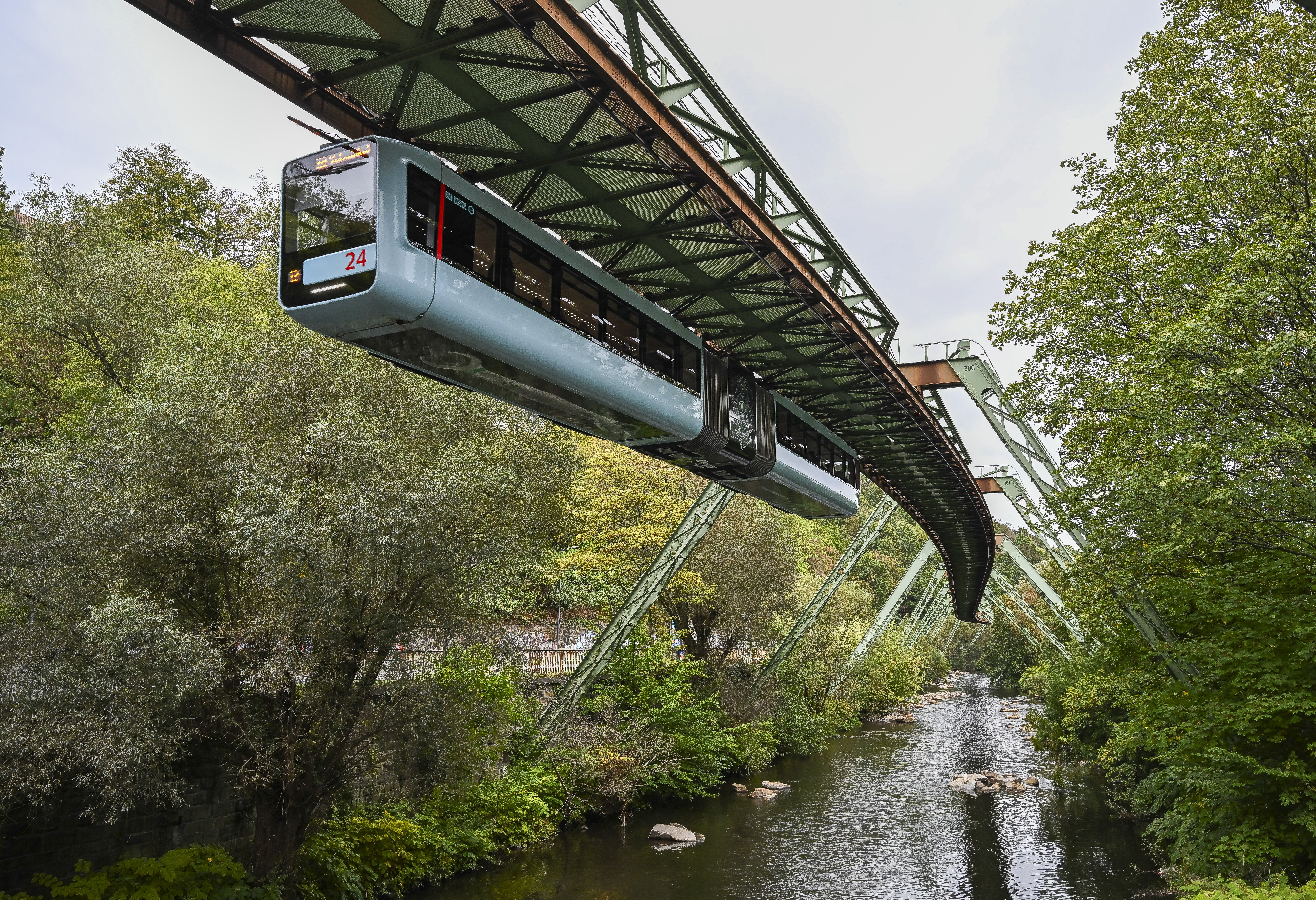 Two tram cars hang beneath a suspended railway above a river.