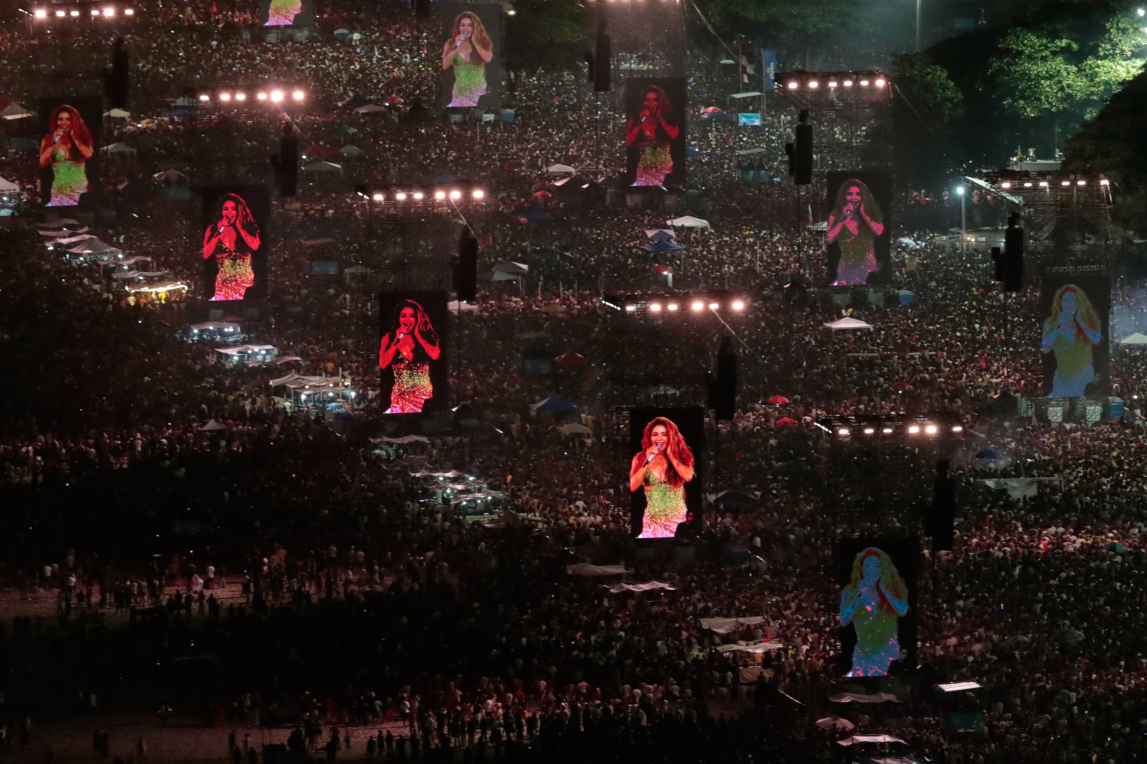More than a dozen tall video screens stand among a large crowd on a beach watching Shakira perform in concert.