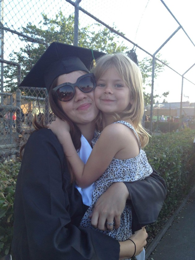 Amber Angel, dressed in a graduation cap and gown, holds her daughter Lennon