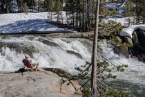 A man reads on the ledge near a stream filled with melting snowpack