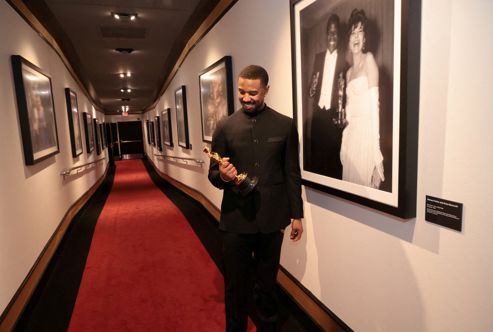 Michael B. Jordan stands in a hallway, posing with his recently-won Oscar award.
