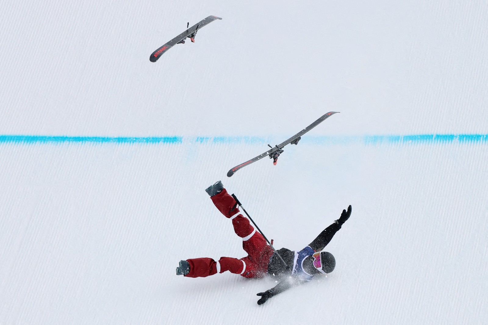 A ski racer falls during a run, their skis flying off into the air.