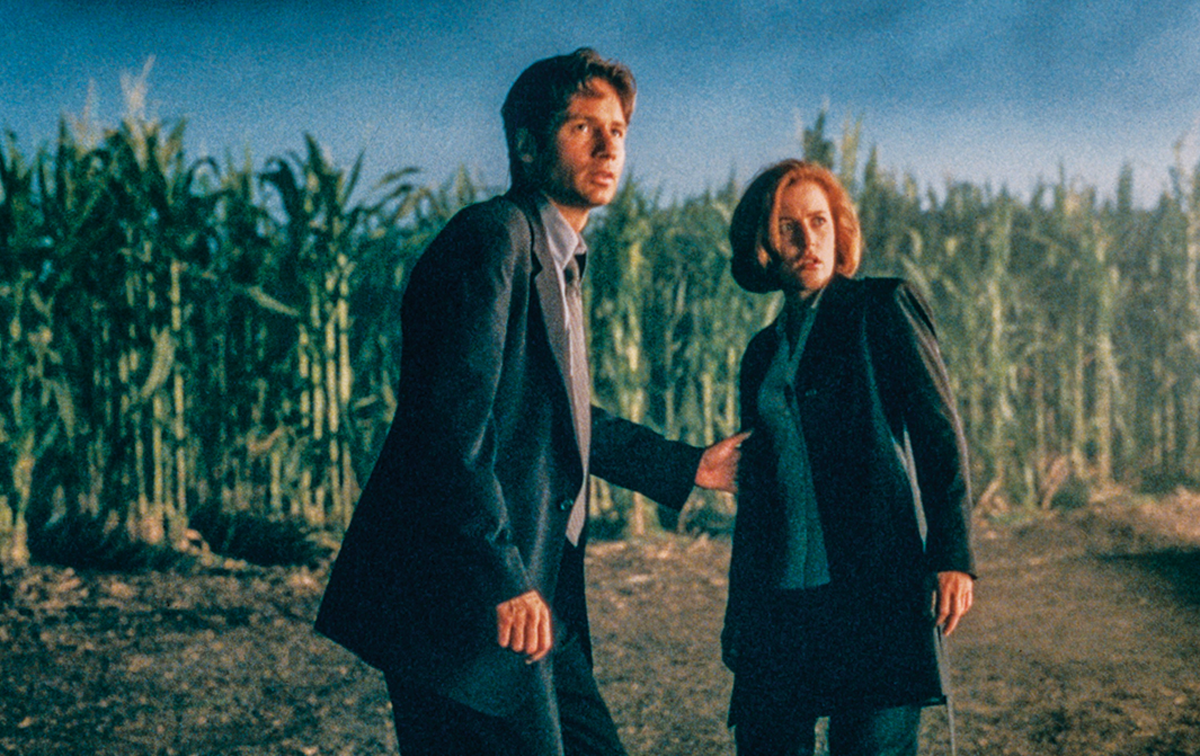 movie still of man and woman in suit looking shocked with corn field behind