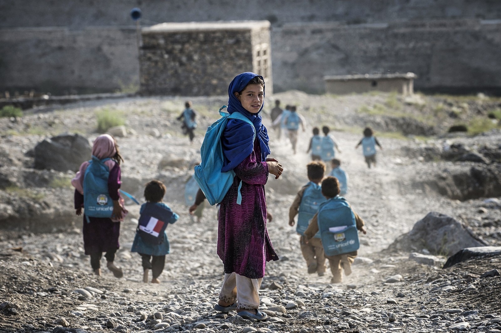 Young students in Afghanistan, wearing backpacks, run along a path.