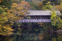 A covered bridge is flanked by autumn leaves beginning to change color along the Contoocook River in Henniker, New Hampshire, on October 6, 2023.