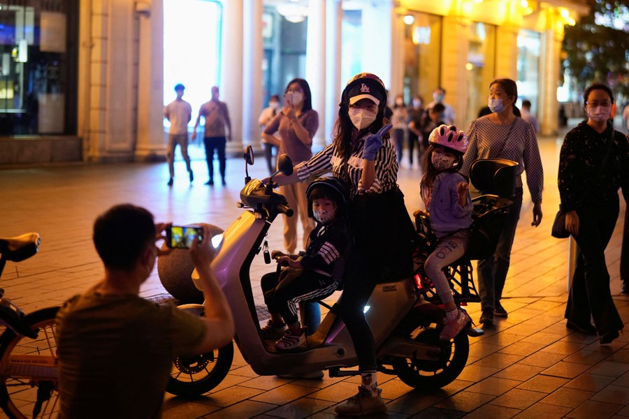 People pose for pictures on a scooter in a shopping plaza.