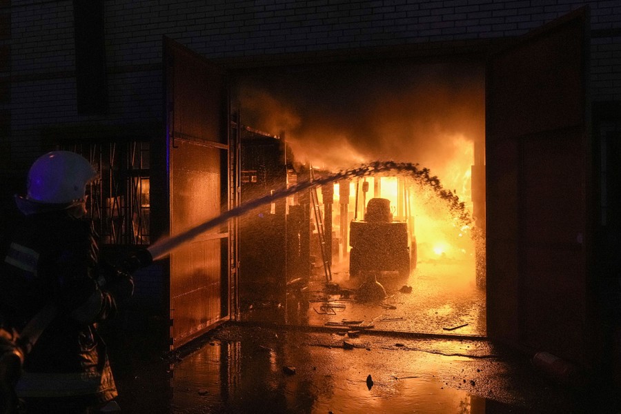Inside a dark hallway, a firefighter spraying water toward a fire at the end of the hallway.
