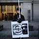 A man dressed in black holds a sign with a symbol for bitcoin