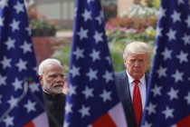 Color photo of Narendra Modi standing next to Donald Trump with three American flags in the foreground