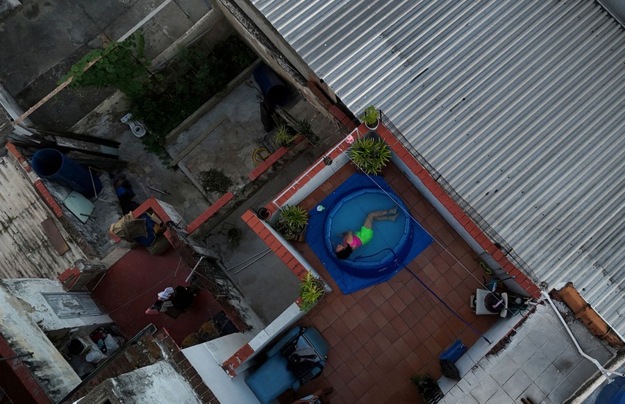 A drone view of a person lying in a small inflatable pool on their back deck.
