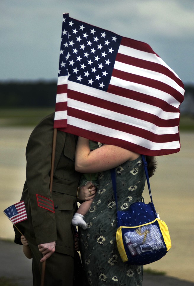 A military husband and wife kissing behind an American flag