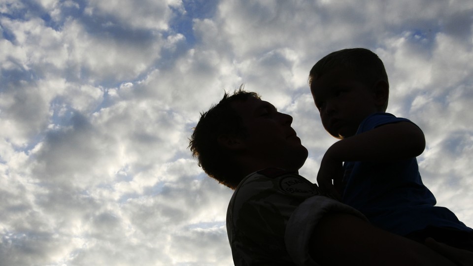 The silhouette of a father holding his son with a cloudy blue sky in the background