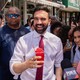 Zohran Mamdani smiling while holding a red slushy, in front of other New Yorkers