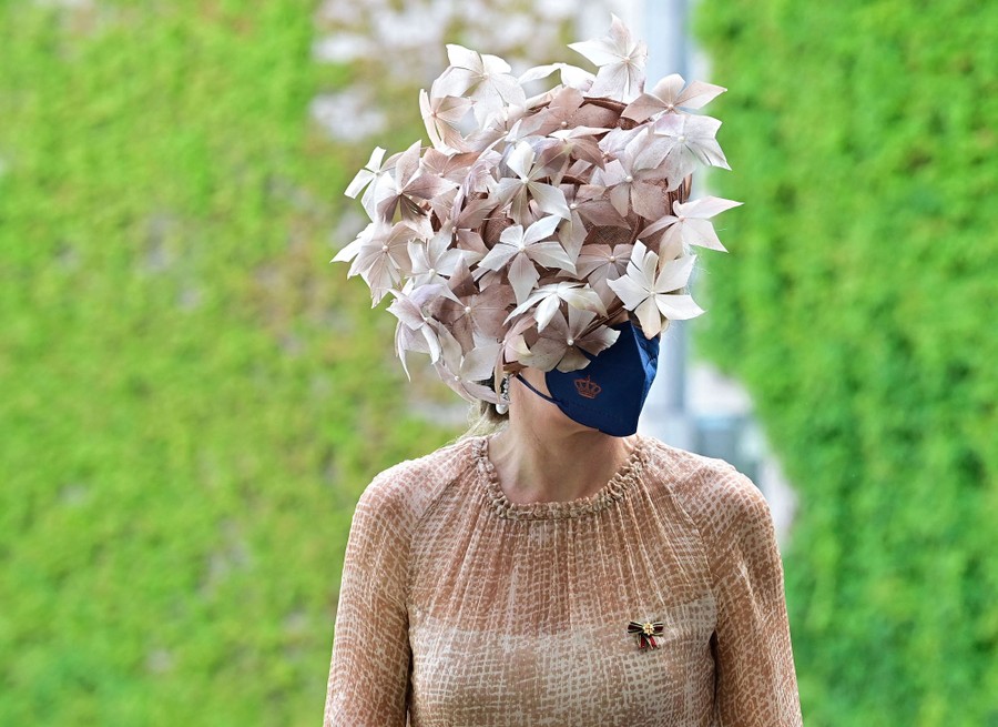 Queen Máxima of the Netherlands is seen wearing an ornate hat and protective mask.