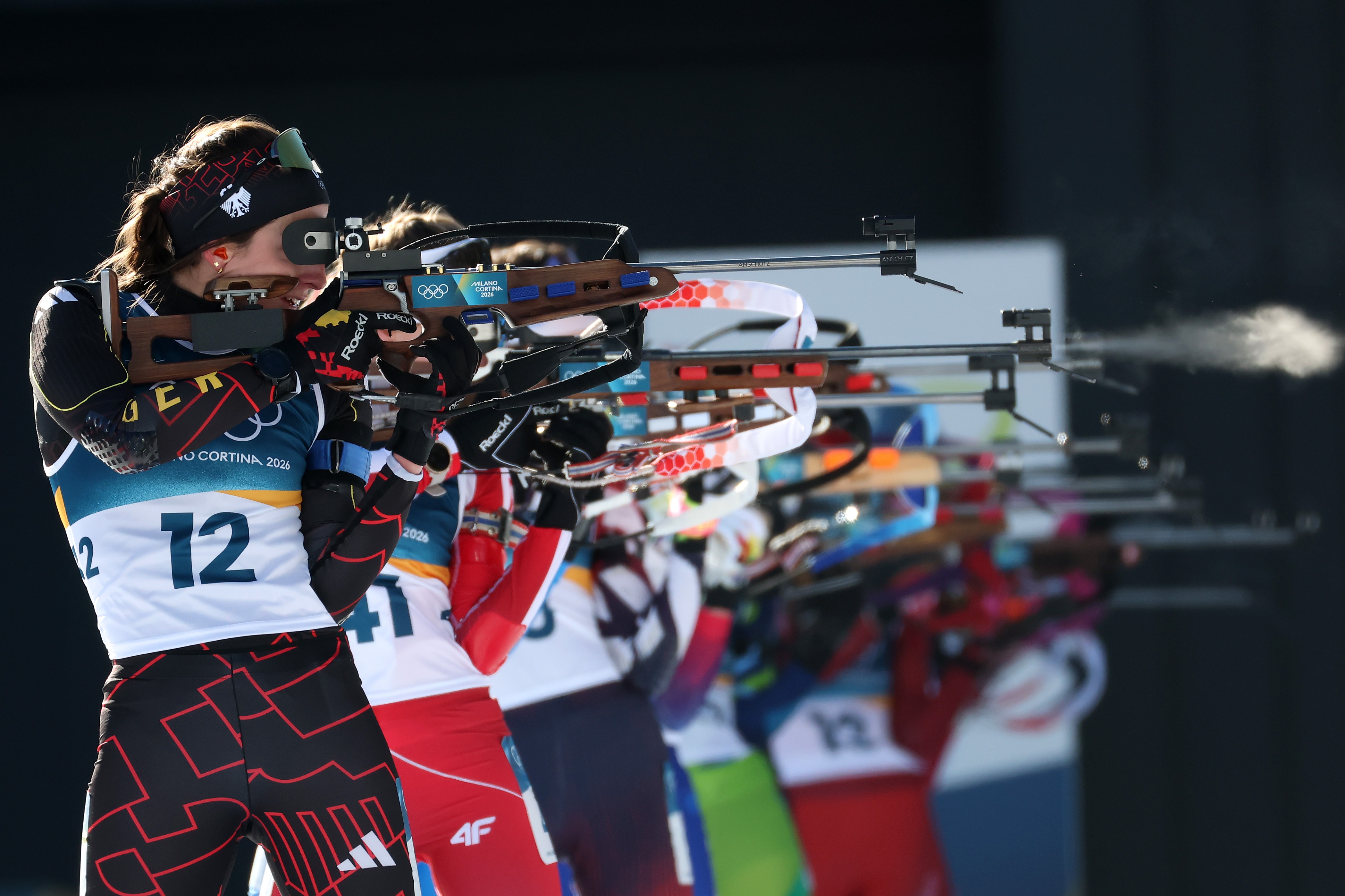 Biathletes stand side-by-side, rifles raised, during a shooting bout.