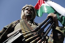 A Houthi supporter against a blue sky with arms