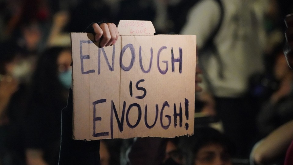 A hand holds up a sign that reads "Enough Is Enough!"
