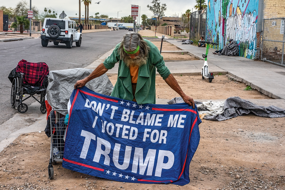 photo of bearded man on side of street holding blue and red "Don't Blame Me I Voted for Trump" flag