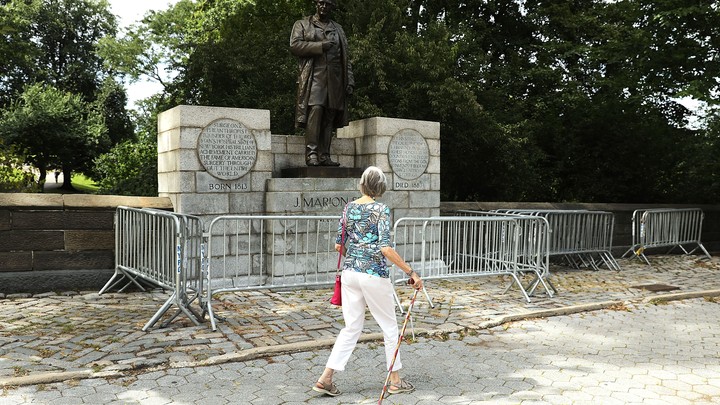 A woman with a cane walks past the J Marion Sims statue in New York's Central Park.