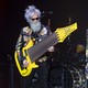 Two musicians perform onstage, with the one on the left playing a gigantic 17-string bass guitar.
