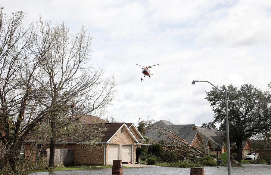 A rescue helicopter lowers a person from a cable above a residential neighborhood.