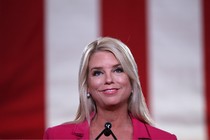 Photo of Pam Bondi smiling at a microphone, with a large American flag behind her