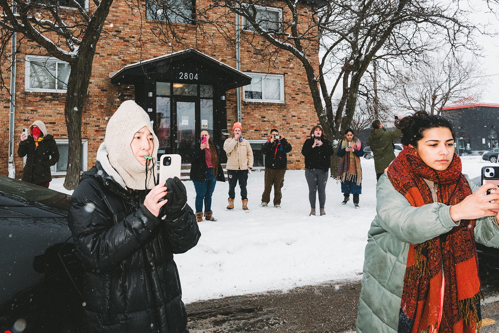 A crowd of people film ICE agents and blow their whistles