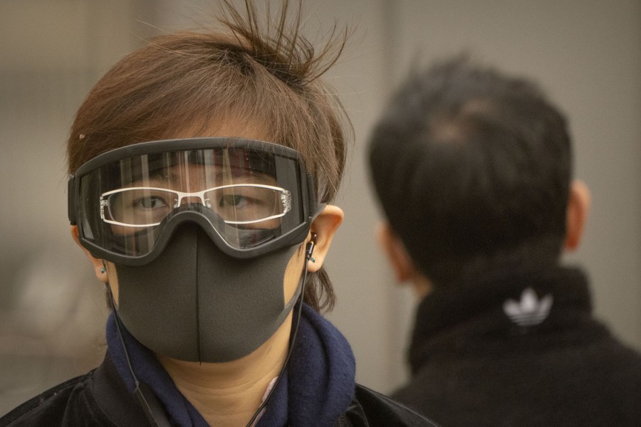 A person wearing a face mask and goggles walks along a street.