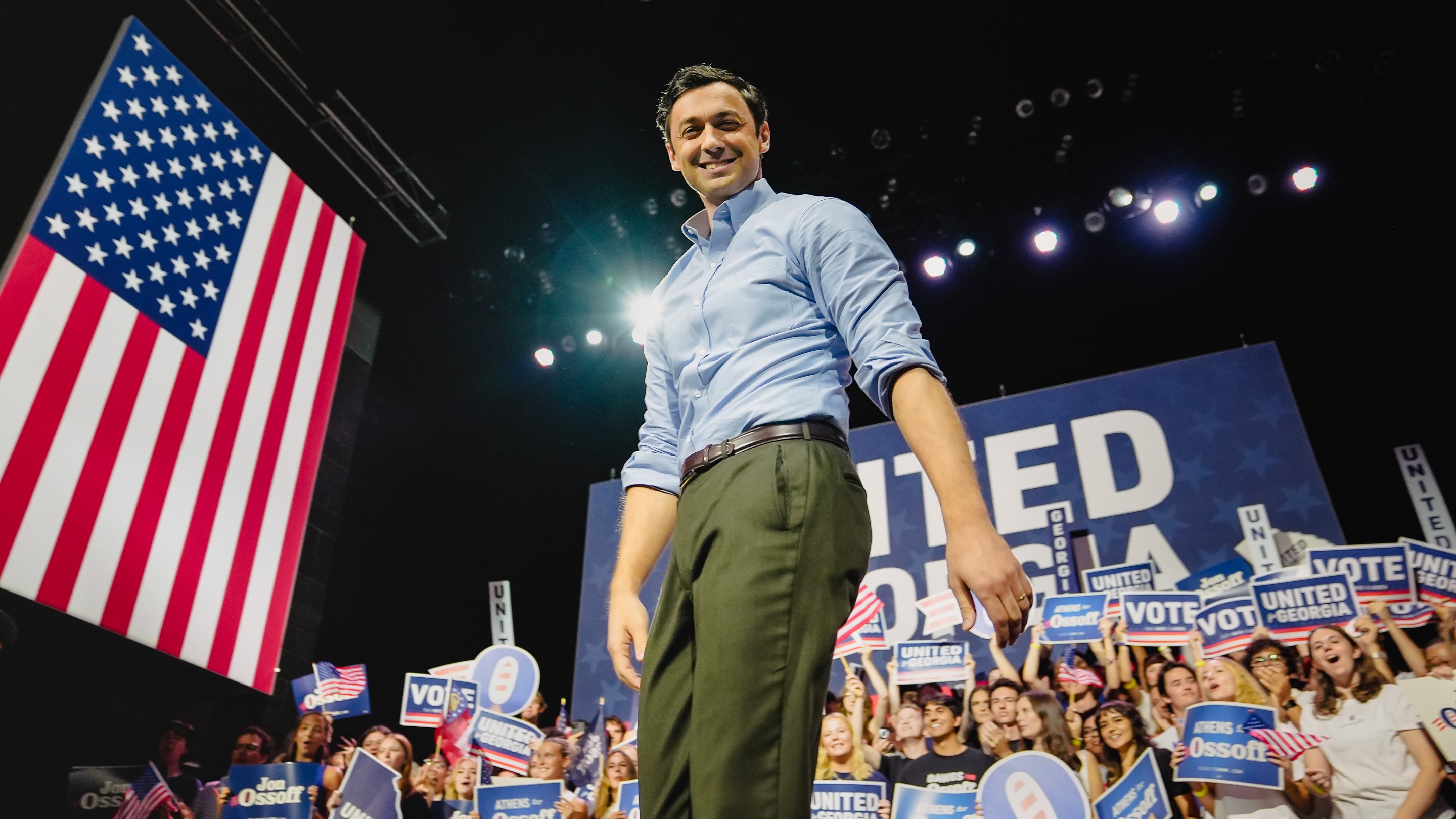 A man stands on stage with an American flag behind him