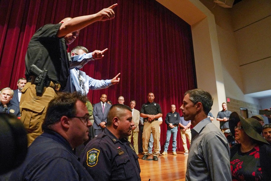 Security officers on and in front of a stage point their hands, attempting to get a man on the floor to leave.