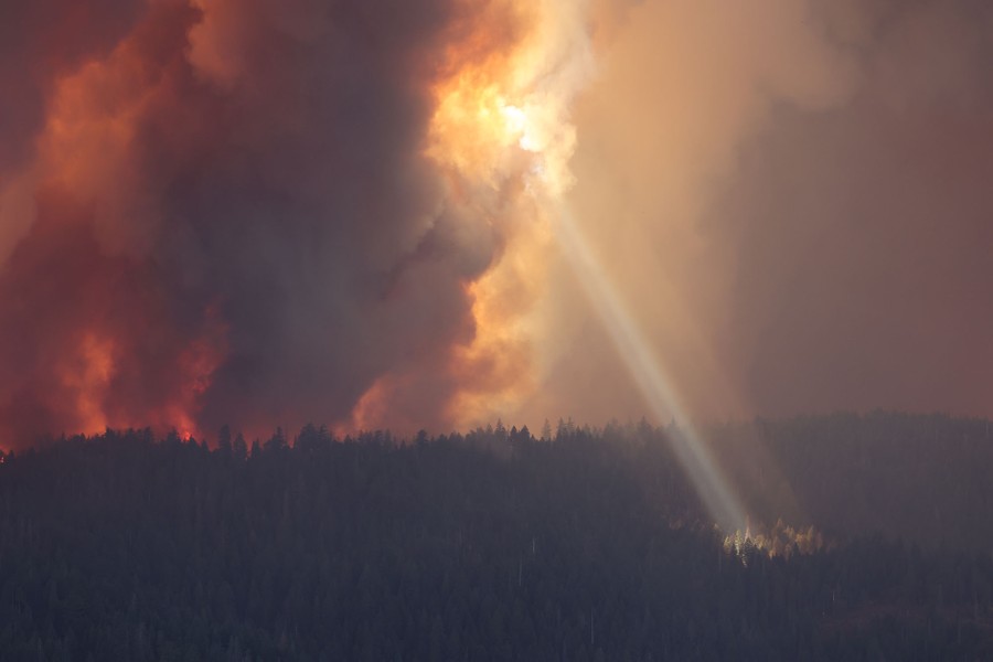 A shaft of sunlight breaks through smoke rising from a large forest fire.