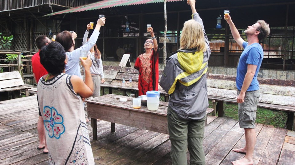 A group of people stands in a circle and raises cups containing a brown liquid.