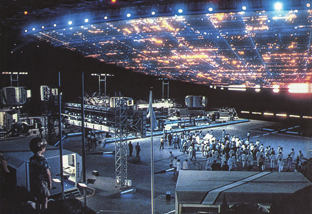 movie still of large crowd of people under brightly lit model of alien spaceship