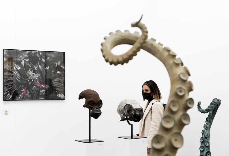 A visitor looks at various sculptures in a white room.