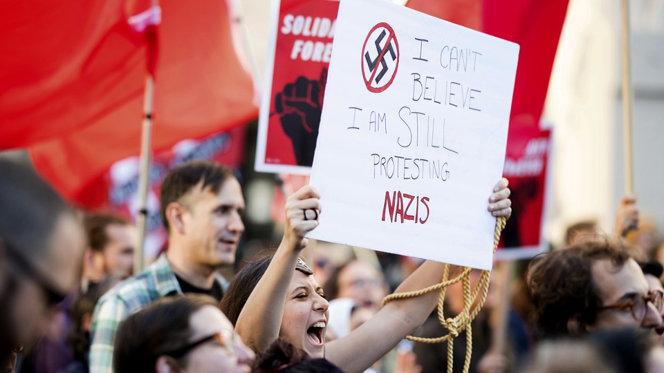 A protestor in Oakland holds a sign that says "I can't believe I'm still protesting Nazis"