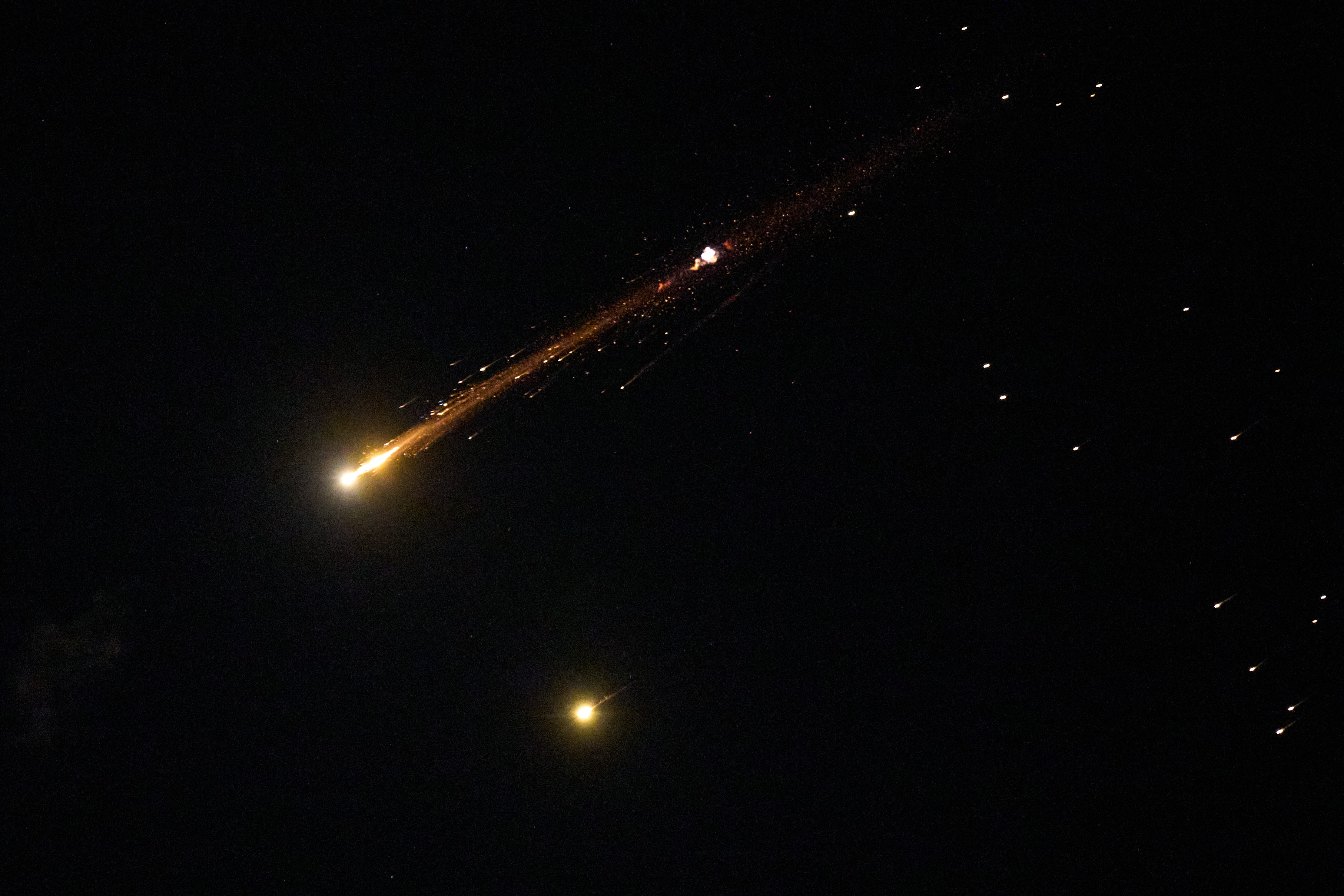 A missile explodes in the night sky, leaving streaks of light.