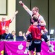 An athlete raises his arm in celebration while being lifted by a coach.