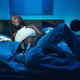 Amaarae in a white crop tank and blue pants, lying on a bed with blue satin sheets in a blue room