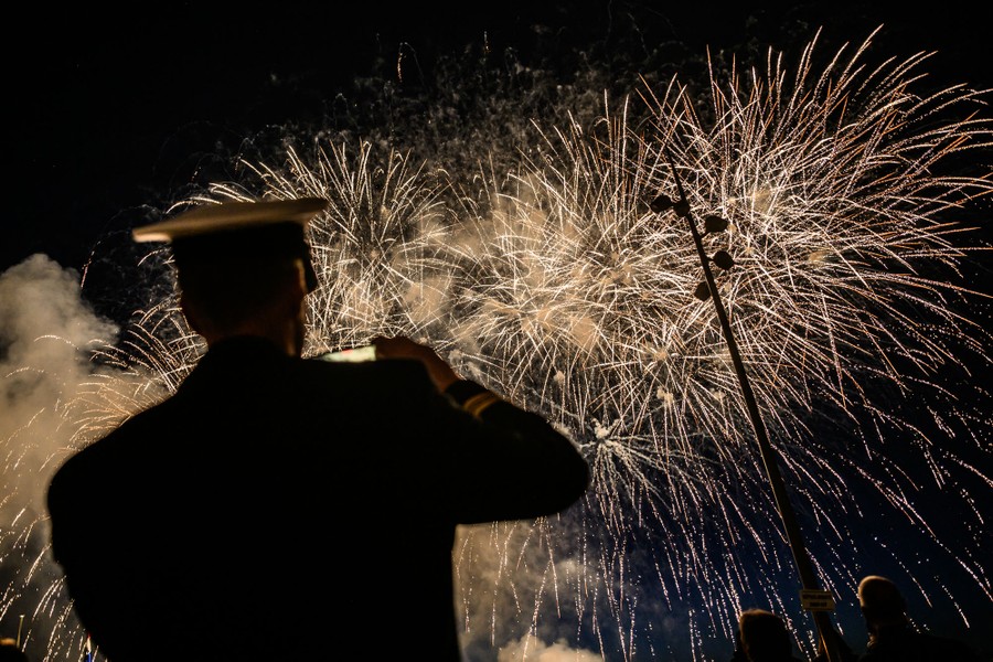 A soldier in dress uniform watches fireworks overhead.