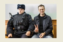 A photo of Alexei Navalny flashing a V sign with his fingers next to a guard