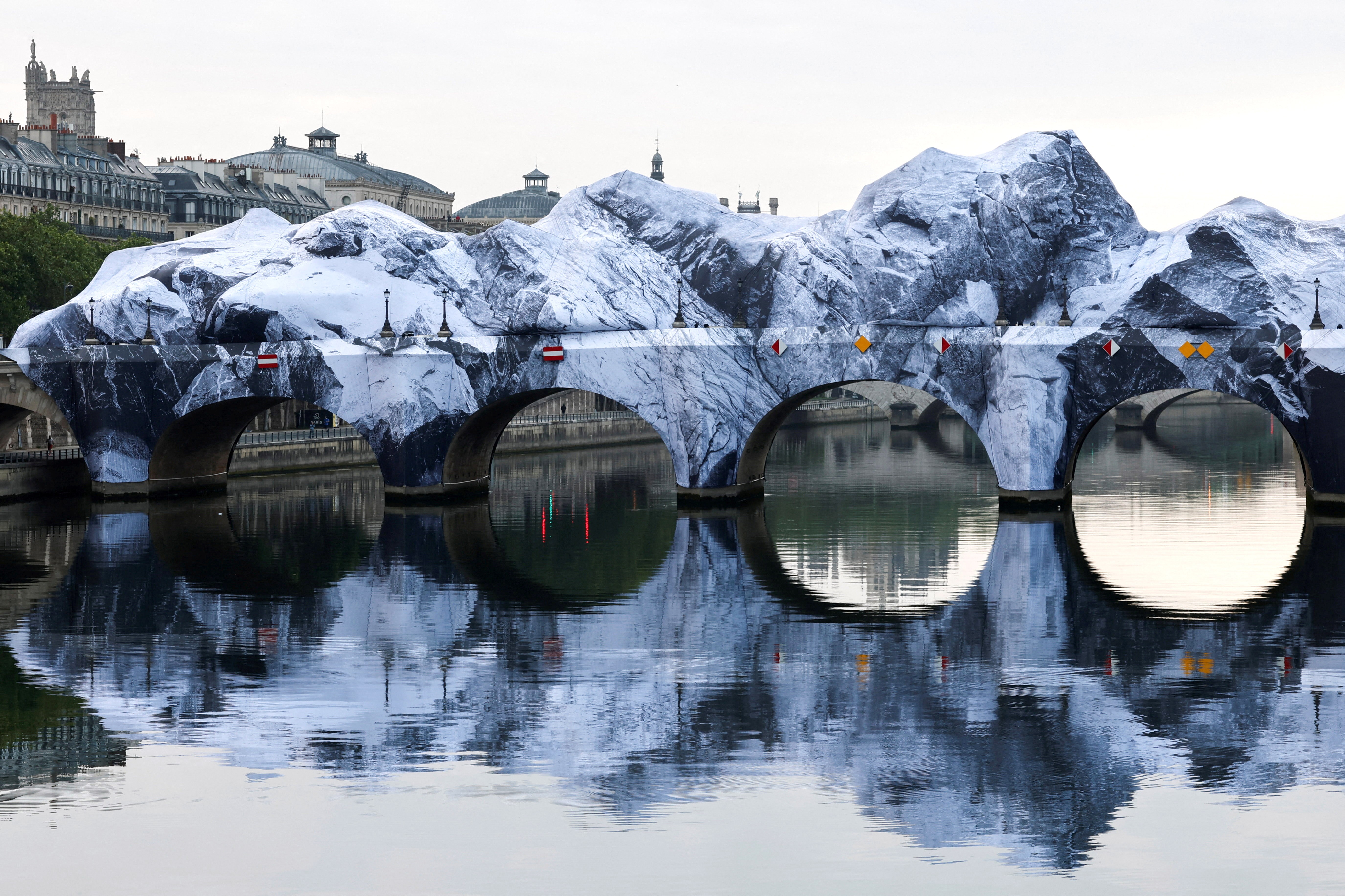 A large inflatable sculpture encompasses a bridge across a river, resembling a large rock formation.